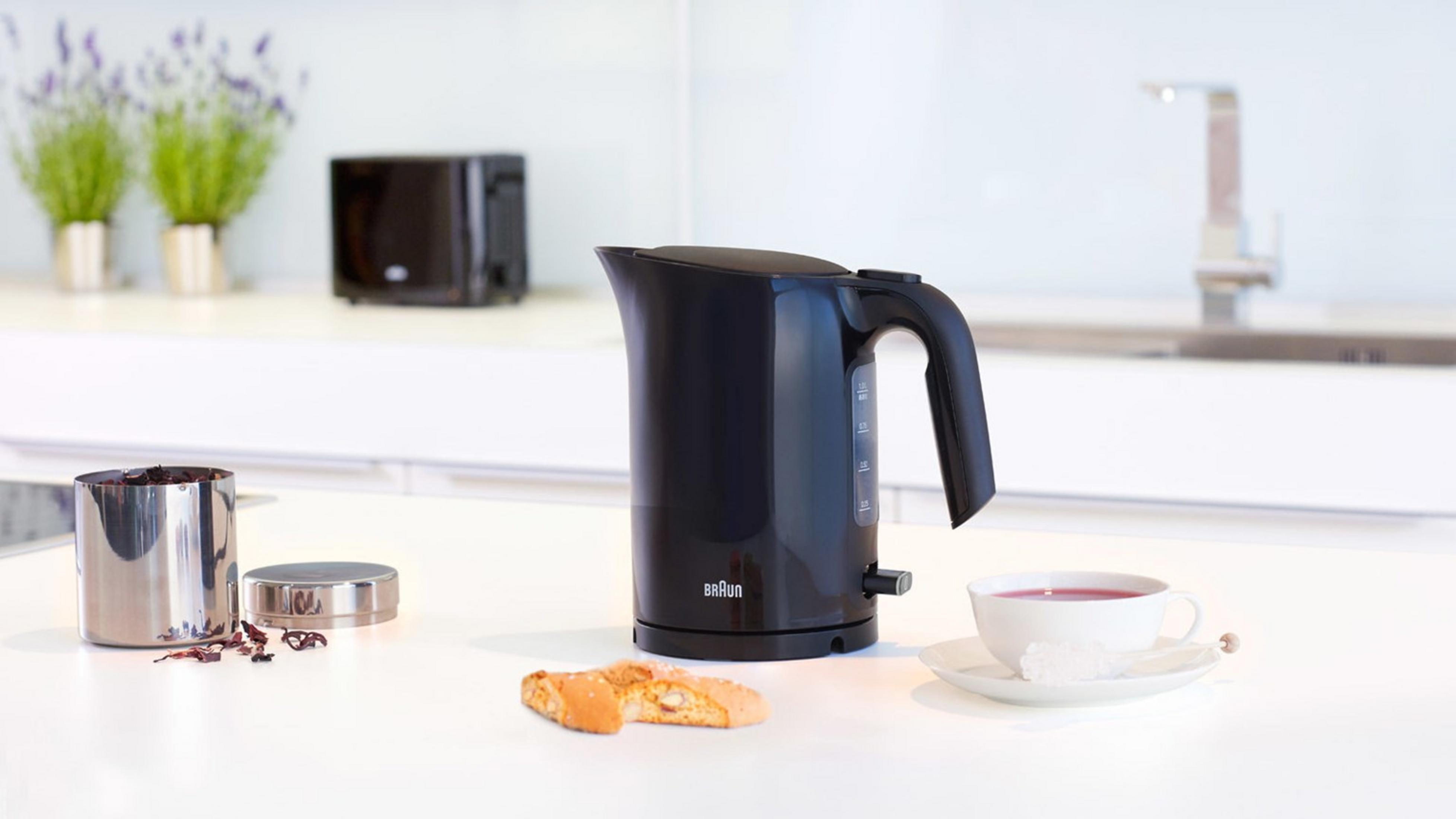 Schwarzer Wasserkocher mit Tasse und Keksen auf einer Küchenarbeitsplatte.