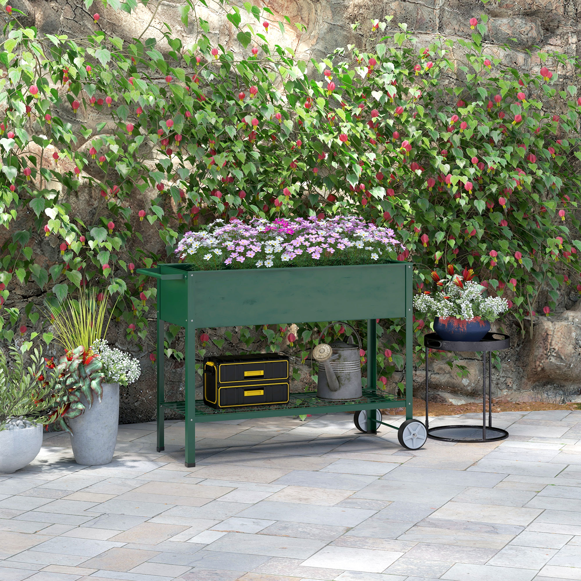 Ein grüner Hochbeet-Pflanzer mit Blumen und Pflanzen steht auf einer gepflasterten Terrasse.