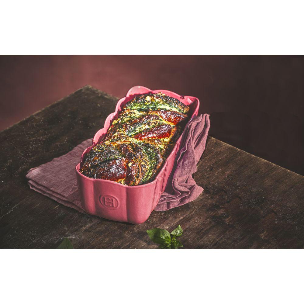 Ein rosa Backblech mit einem gebackenen Brot mit Kräutern und roten Beeren.