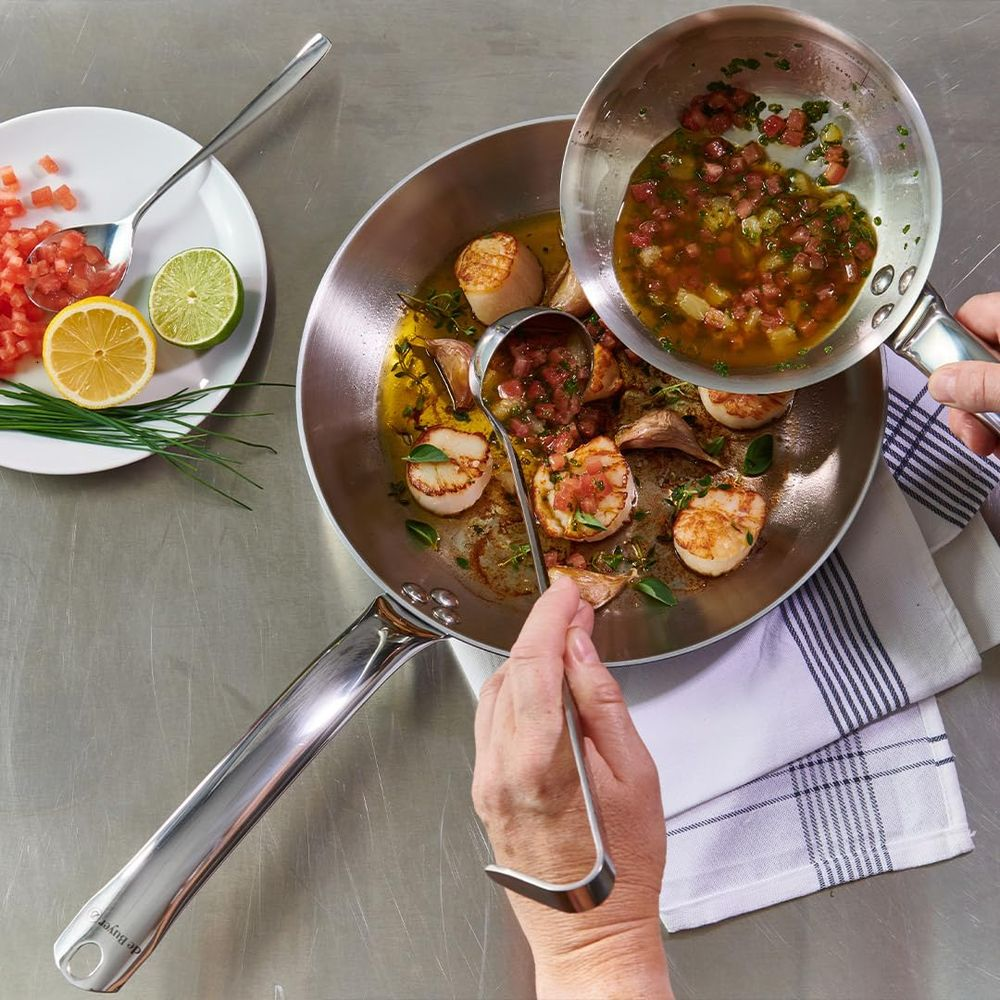Des noix de Saint-Jacques cuisent dans une poêle avec tomates et herbes.