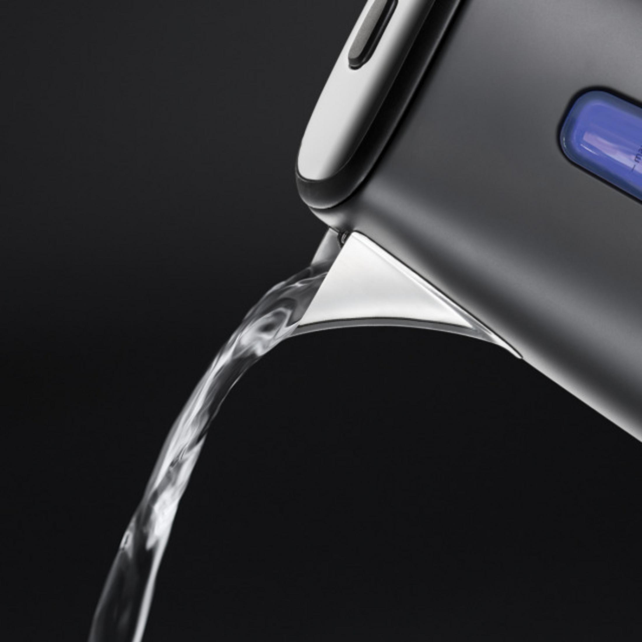 Woda płynie z ciemnego czajnika z srebrną wylewką na czarnym tle.