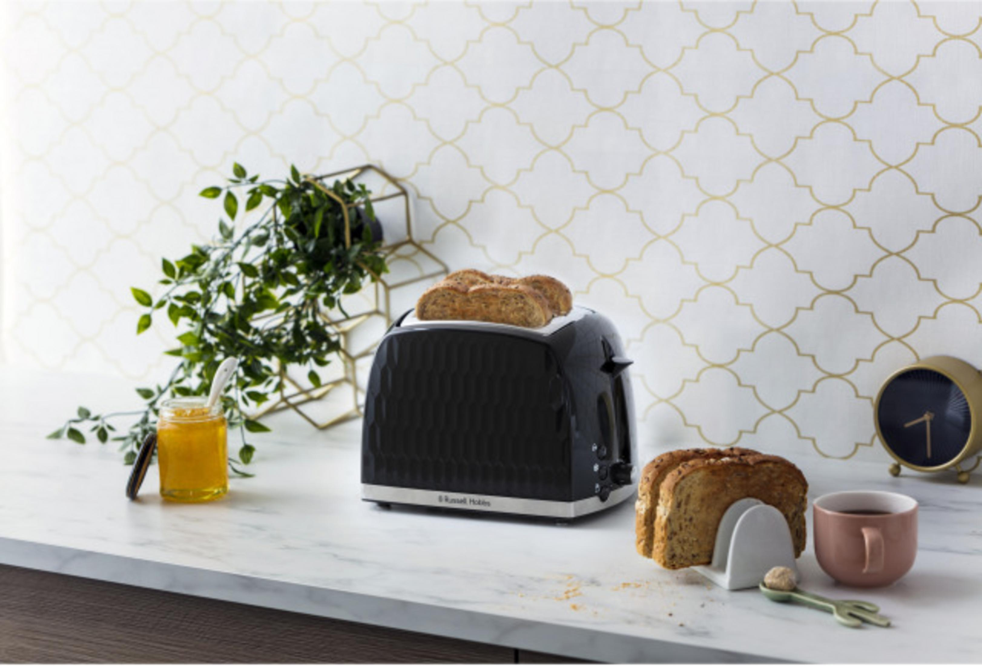 Ein schwarzer Toaster mit Toastbrot, Marmelade, einer Tasse und einer Uhr.