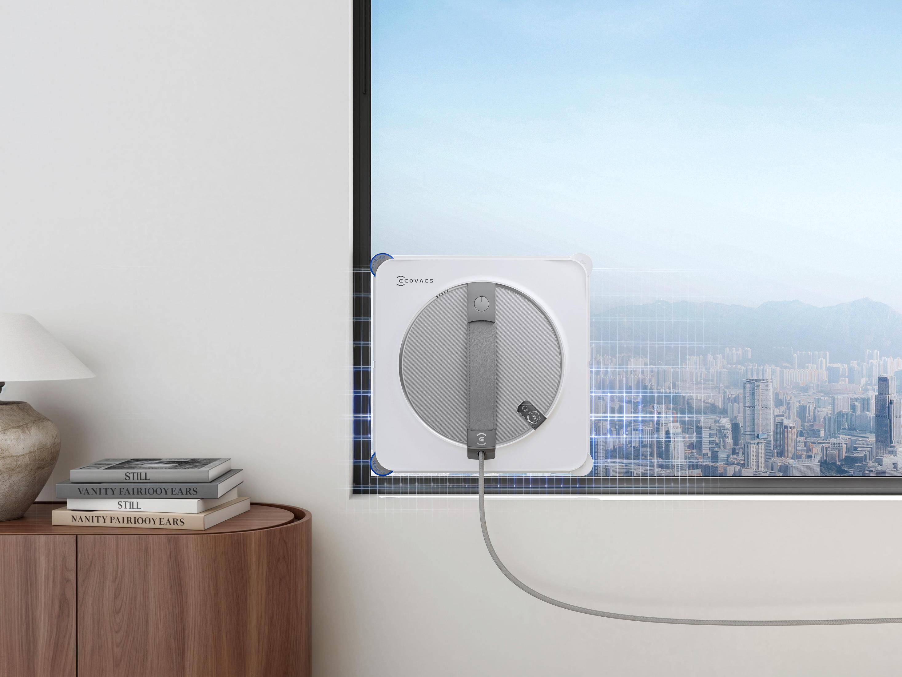 Biały robot do mycia okien przyczepiony do okna z widokiem na miasto.