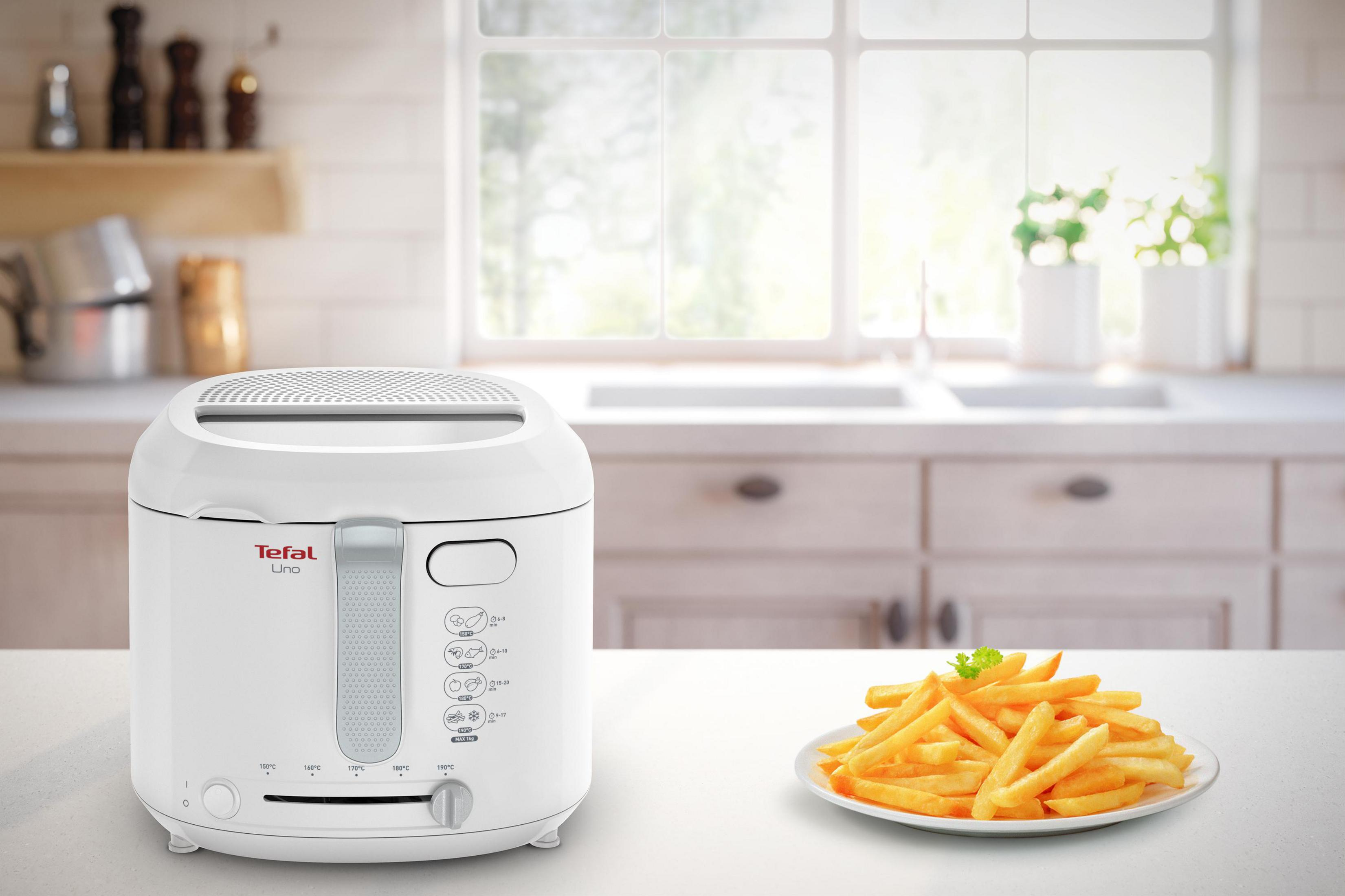Una freidora blanca junto a un cuenco de patatas fritas en una cocina.
