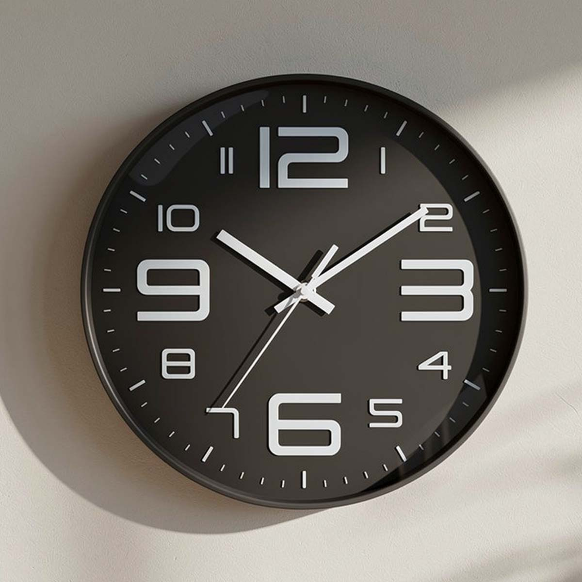 Eine schwarze Wanduhr mit weißen Ziffern und Zeigern hängt an einer hellgrauen Wand.