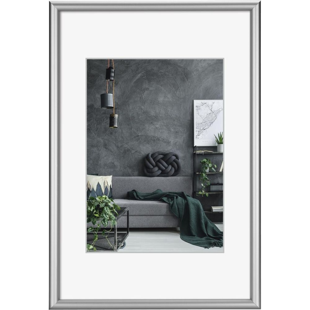 Canapé gris avec couverture verte, coussins et plantes sur mur sombre.
