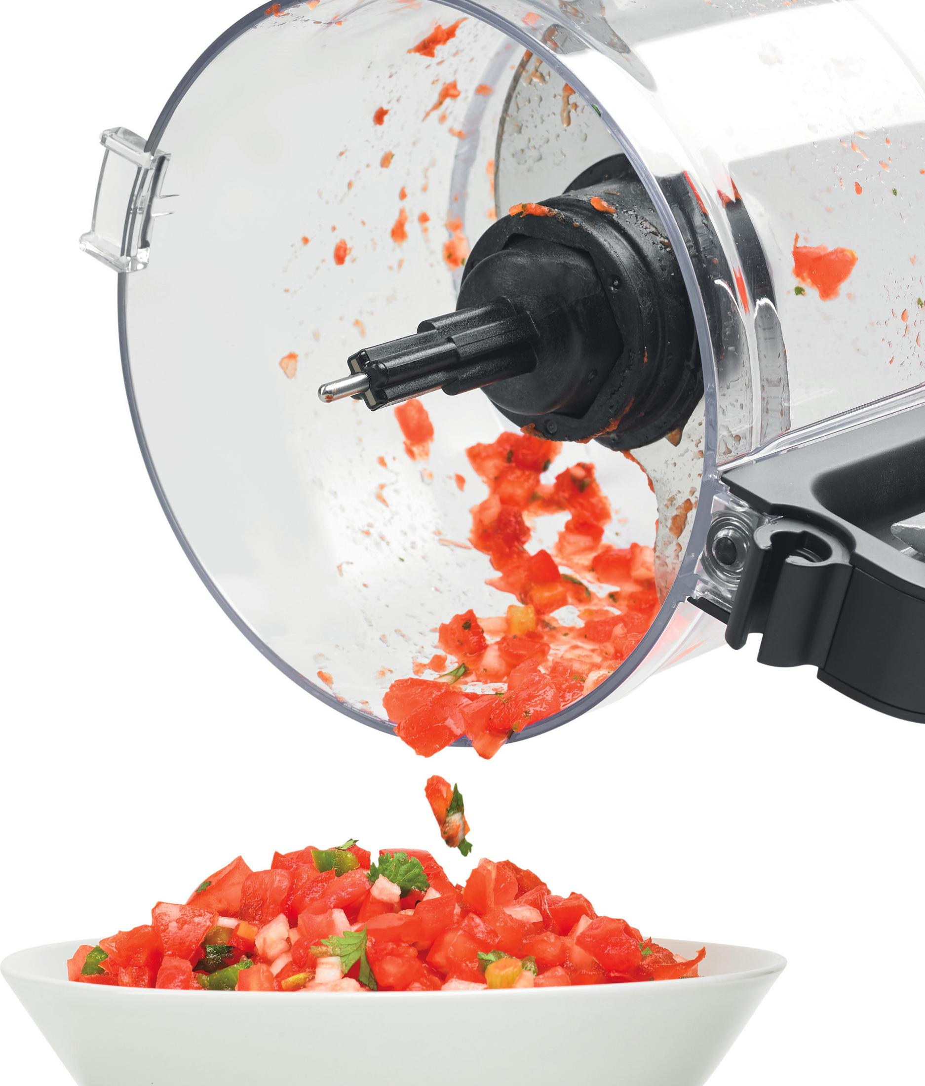 Pomodori tritati cadono da un robot da cucina in una ciotola bianca.