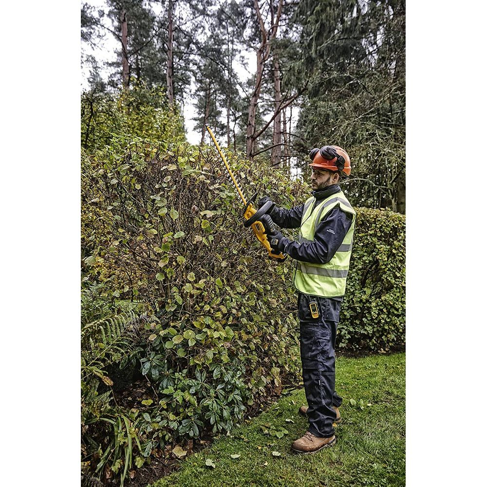 Mann mit Heckenschere schneidet Hecke. Er trägt Helm, Weste und Arbeitshose.