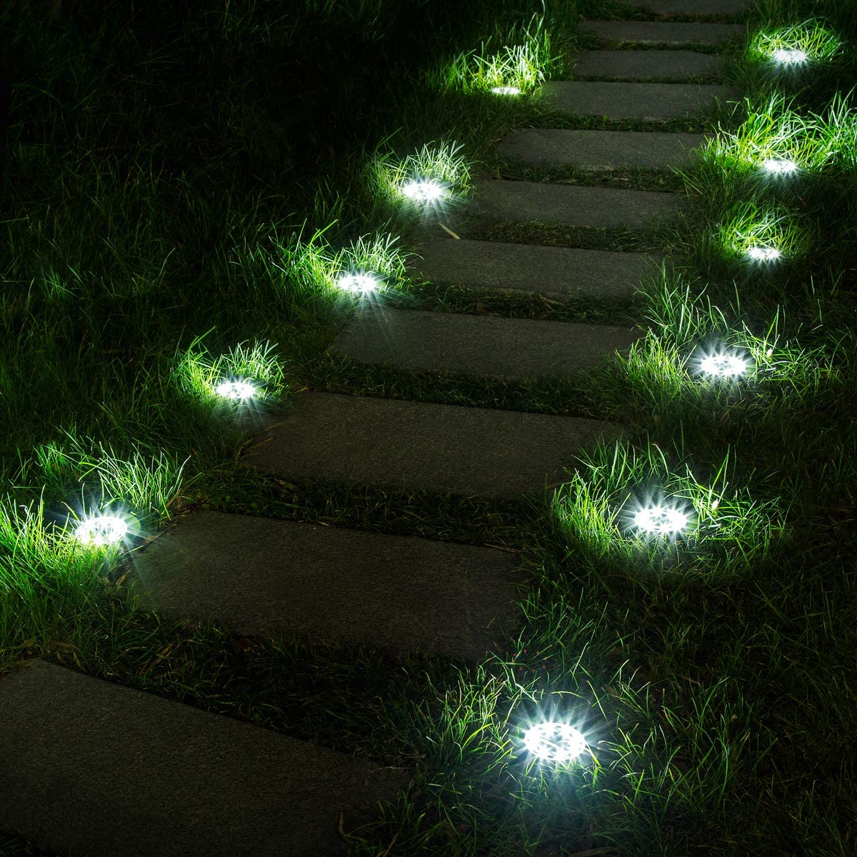 Steinweg im Gras bei Nacht, beleuchtet von Bodenspots.