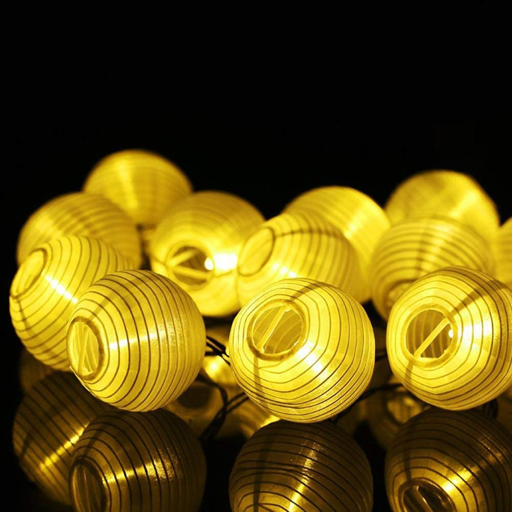 Gelbe Lichterketten mit Papierlaternen vor schwarzem Hintergrund.