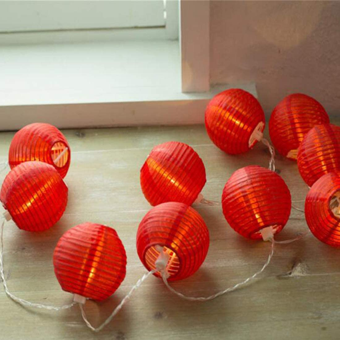Eine Lichterkette aus kleinen, roten, runden Papierlaternen mit weißen Kabeln auf Holz.