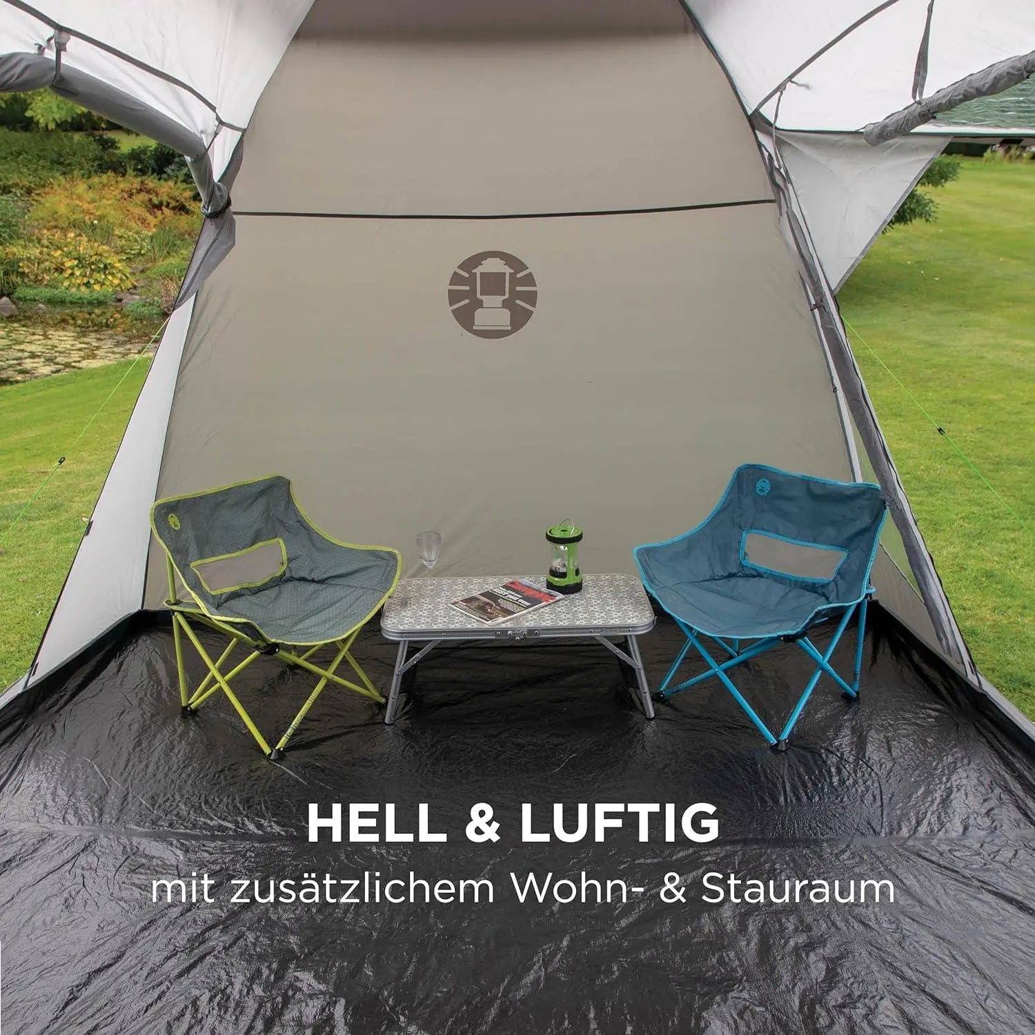 Zwei Campingstühle und ein Tisch stehen in einem hellen Zelt mit Blick auf Grün.