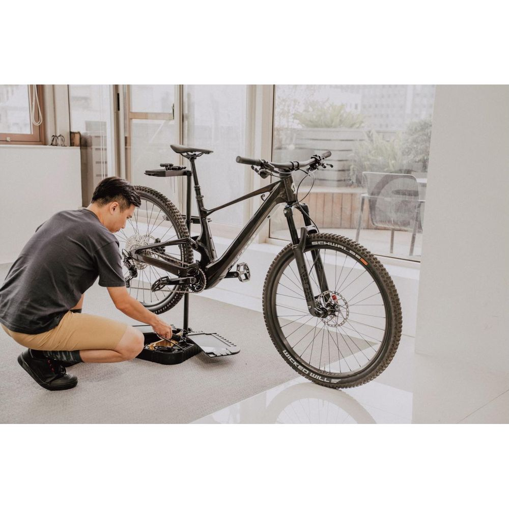 Mann repariert schwarzes Fahrrad auf einem Ständer vor einem Fenster.