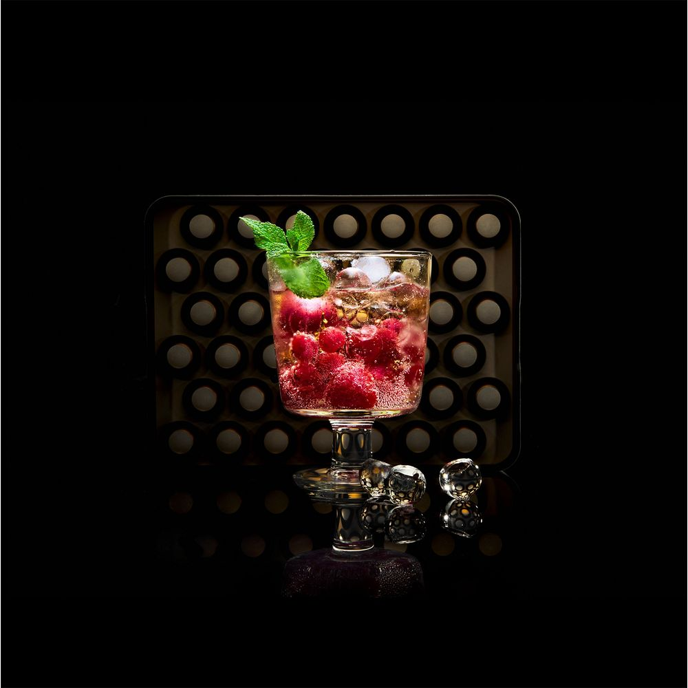 Un verre de boisson aux framboises avec glaçons et menthe sur fond noir.