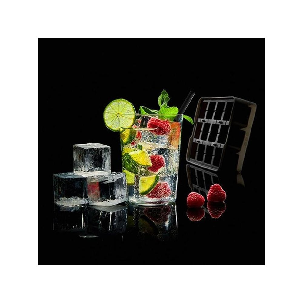 Un bicchiere con un drink, fette di lime, lamponi, menta, cubetti di ghiaccio e uno stampo per cubetti di ghiaccio.