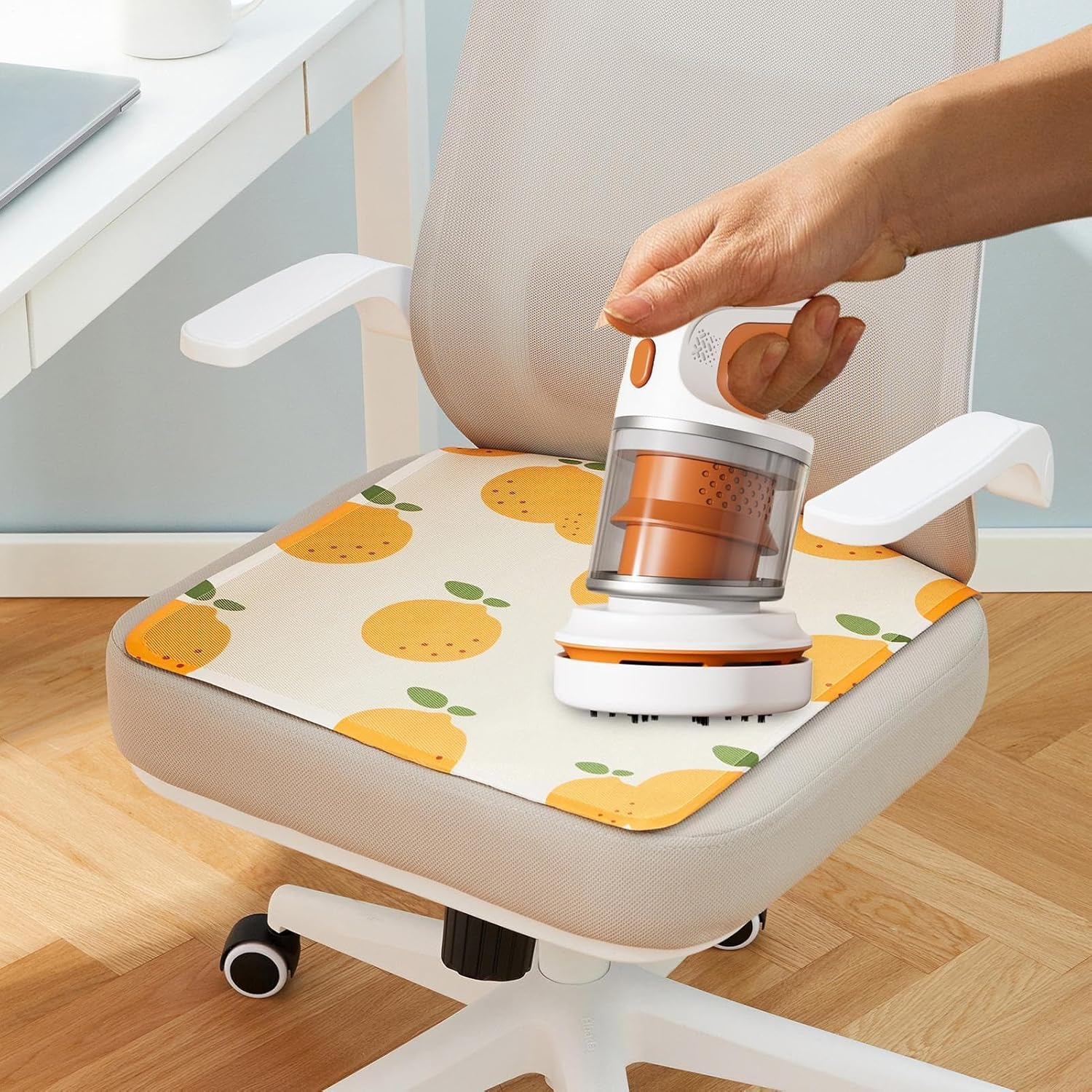 Eine Hand benutzt einen kleinen orange-weißen Staubsauger auf einem Bürostuhl mit Orangenmuster.