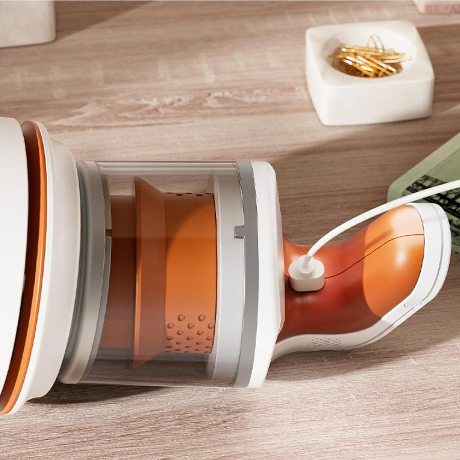 Ein weißer und orangefarbener Mini-Staubsauger mit transparentem Schlauch auf einem Holztisch.