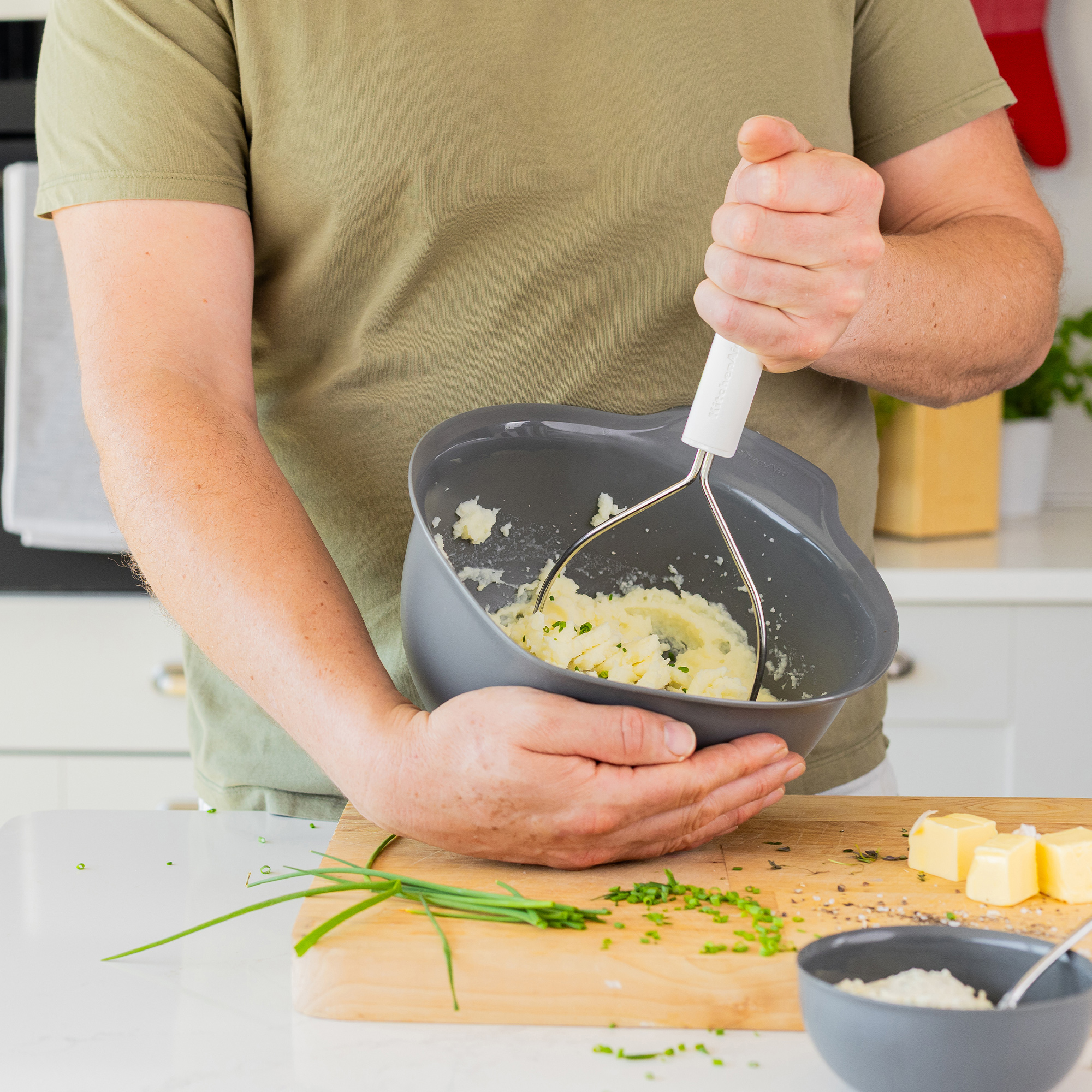 Eine Person zerdrückt Kartoffelpüree in einer Schüssel mit einem Kartoffelstampfer.