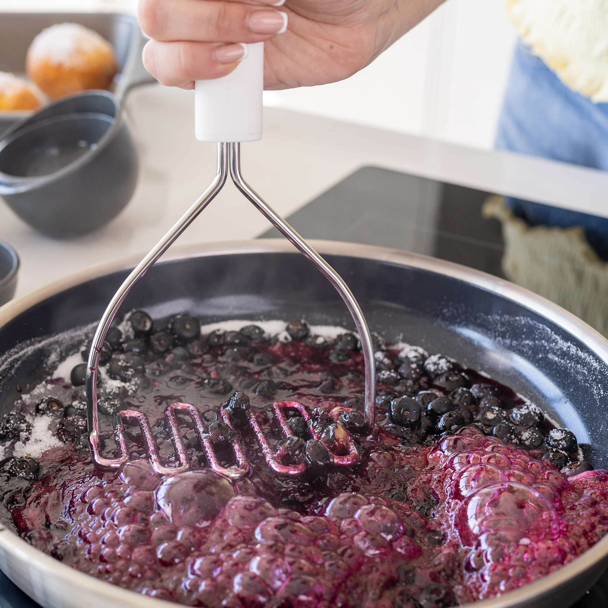 Blaubeeren und Zucker kochen in einer Pfanne, zerdrückt mit einem Stampfer.