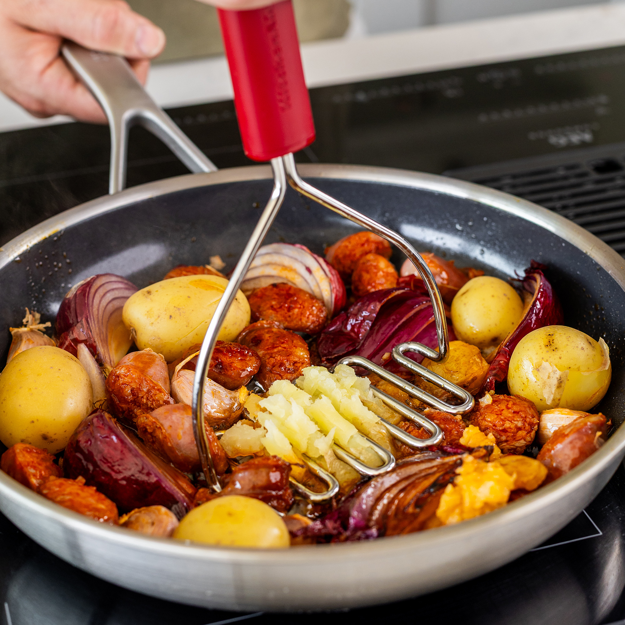 Kartoffeln, Zwiebeln und Wurst werden in einer Pfanne zerdrückt.