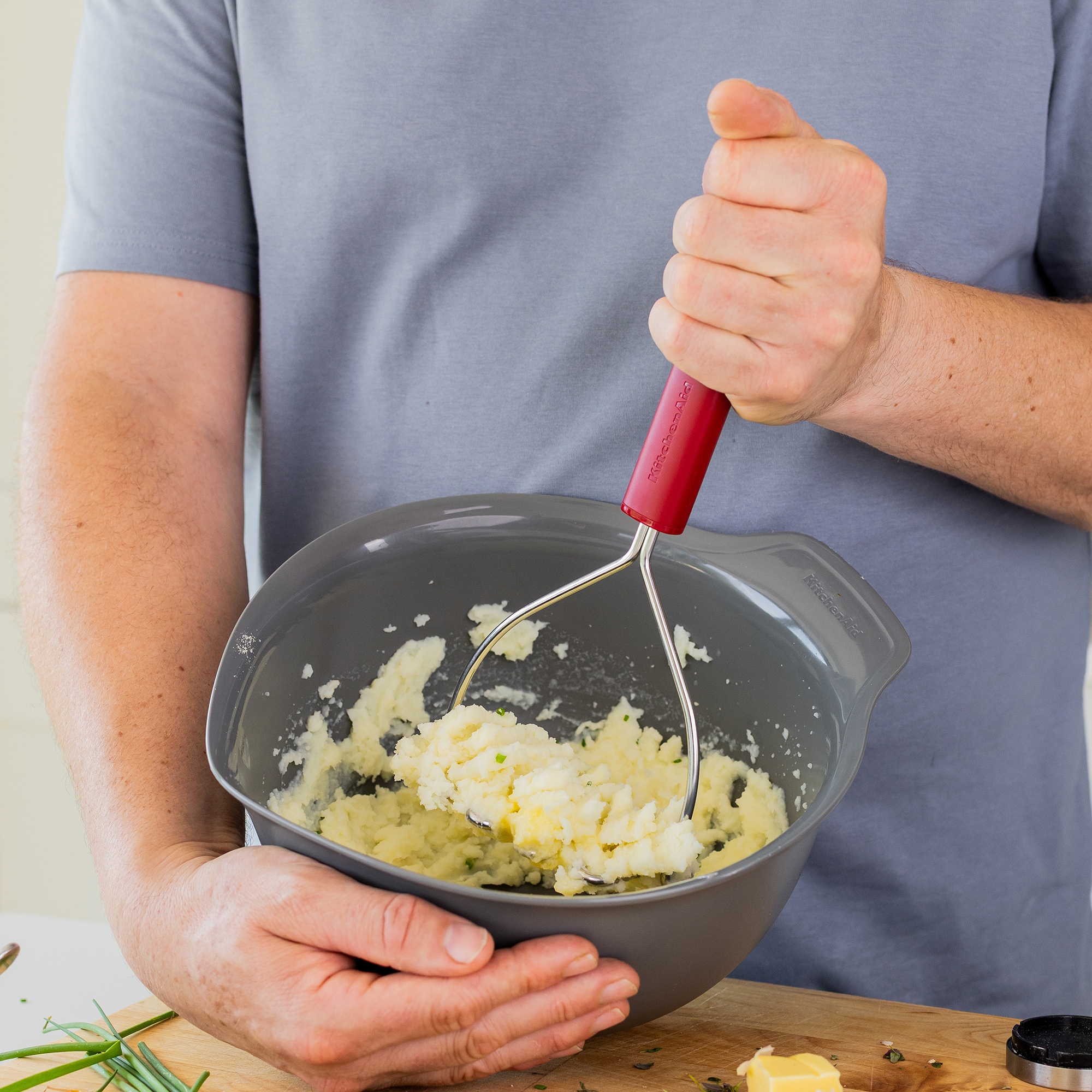 Eine Person zerdrückt Kartoffelpüree in einer Schüssel mit einem Kartoffelstampfer.