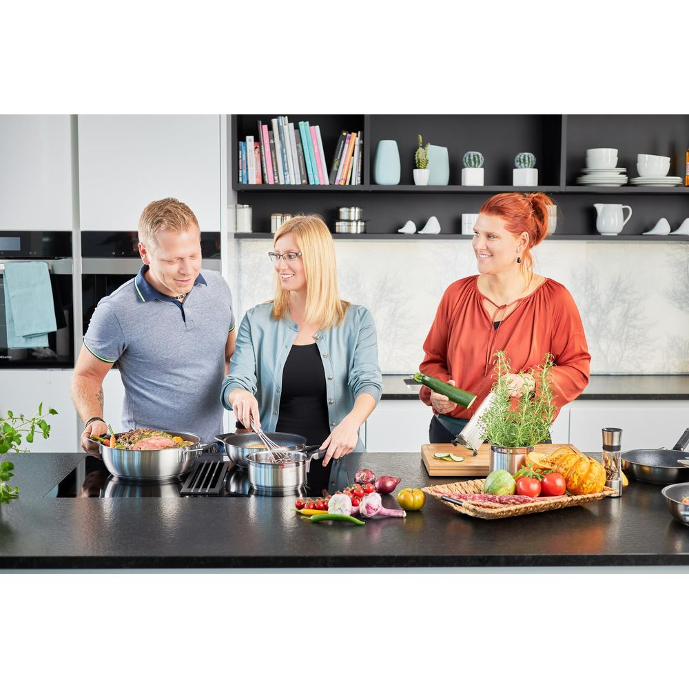 Trois personnes cuisinent dans une cuisine moderne. Elles se tiennent à un comptoir avec de la nourriture.