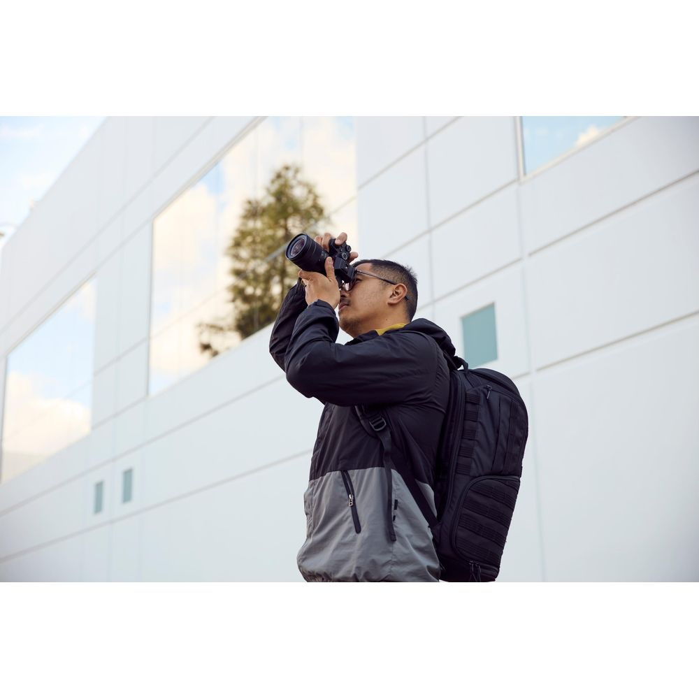 Mężczyzna z plecakiem robi zdjęcie aparatem przed nowoczesnym budynkiem.