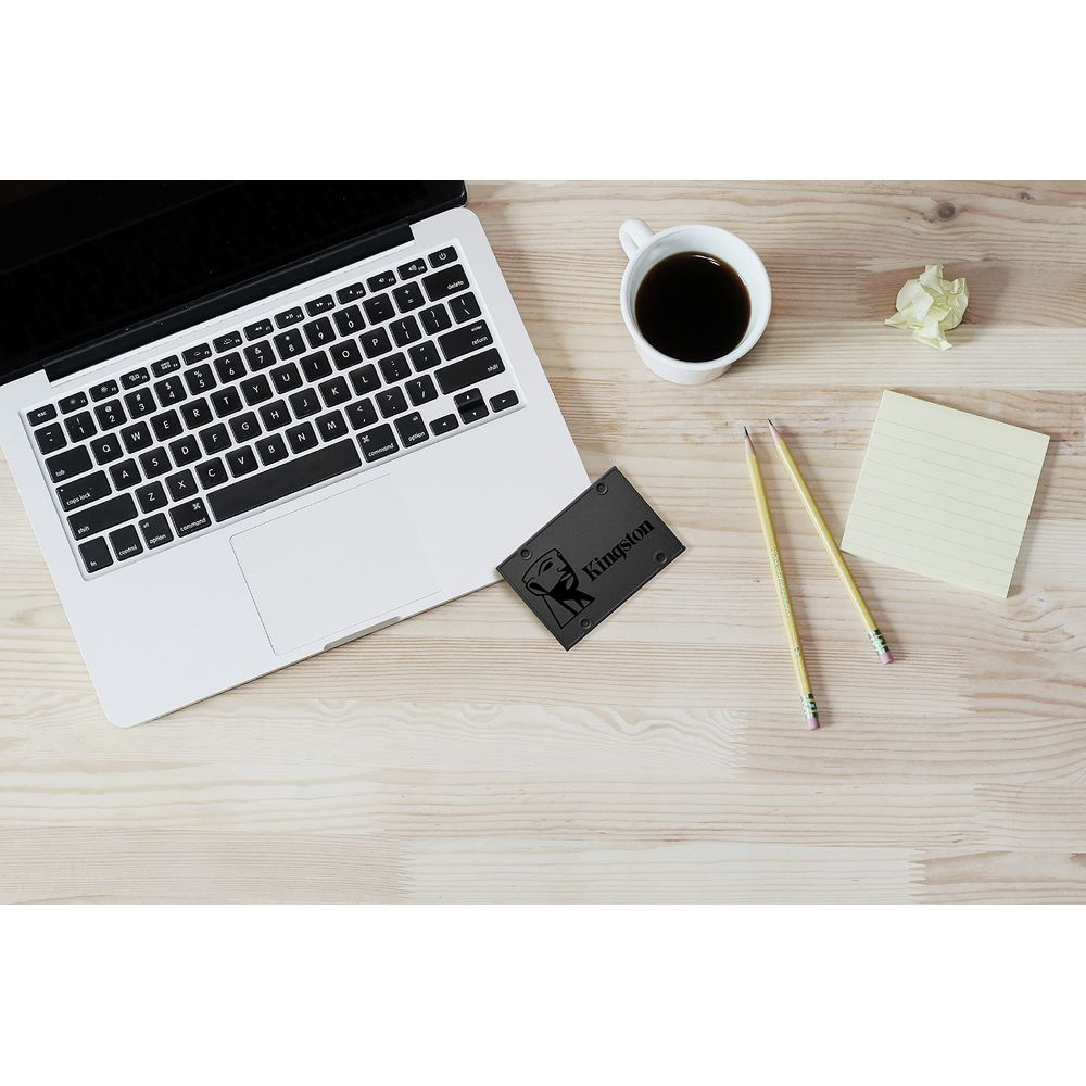 Ein Laptop, Kaffee, Kingston SSD und Bleistifte auf einem Holztisch.