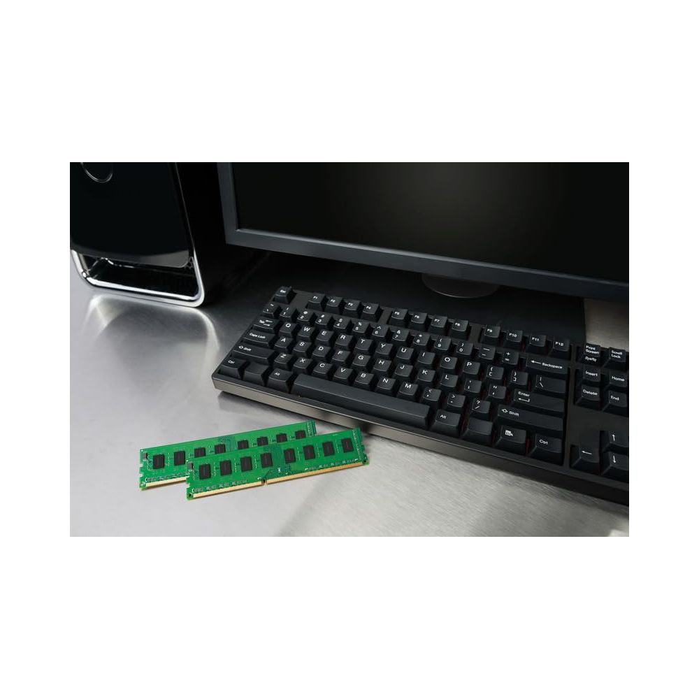 Dwa zielone moduły RAM leżą przed klawiaturą i monitorem komputera.