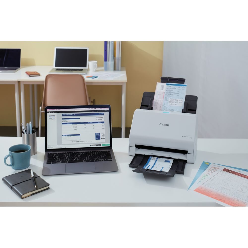 Biały skaner Canon skanuje dokumenty obok laptopa wyświetlającego fakturę.