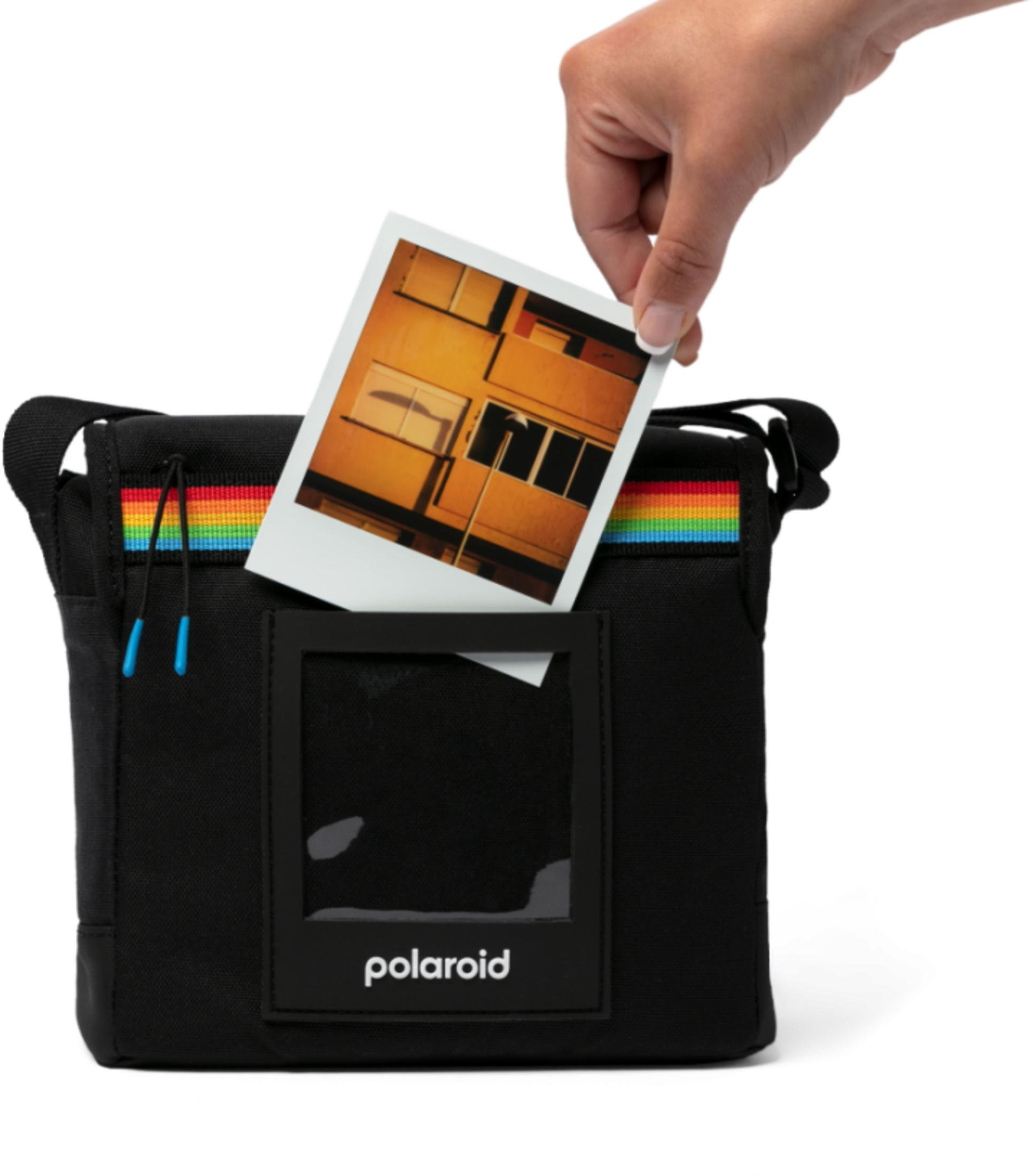 Una mano inserisce una foto in una borsa nera con cinturino arcobaleno.