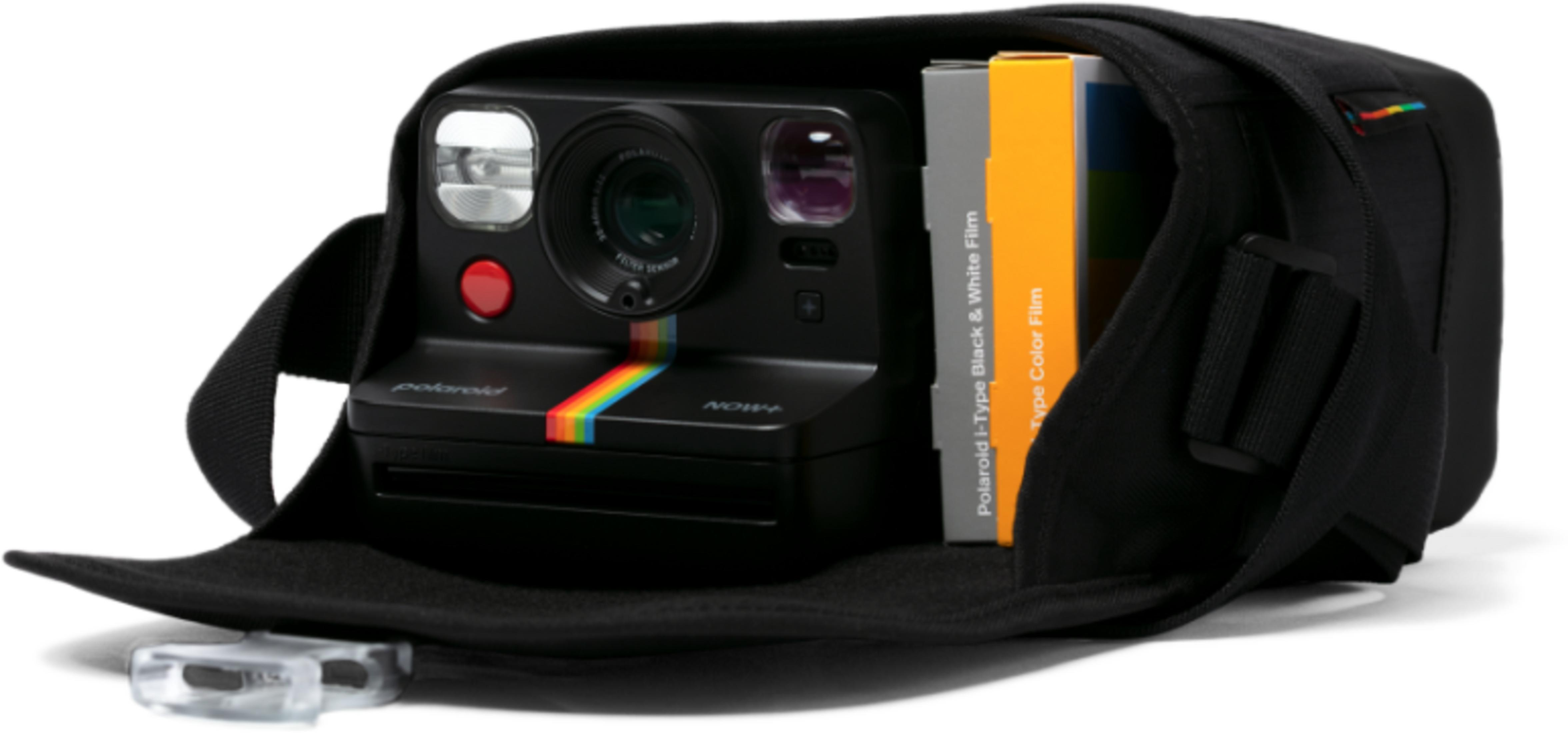 Fotocamera Polaroid nera con striscia arcobaleno in borsa aperta con pacchi di pellicole.
