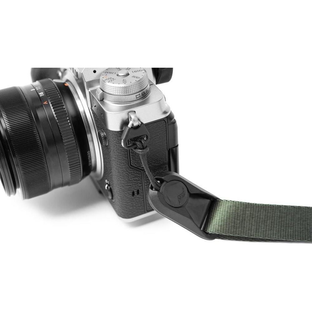 Primo piano di una fotocamera argentata con obiettivo nero e cinghia verde oliva.