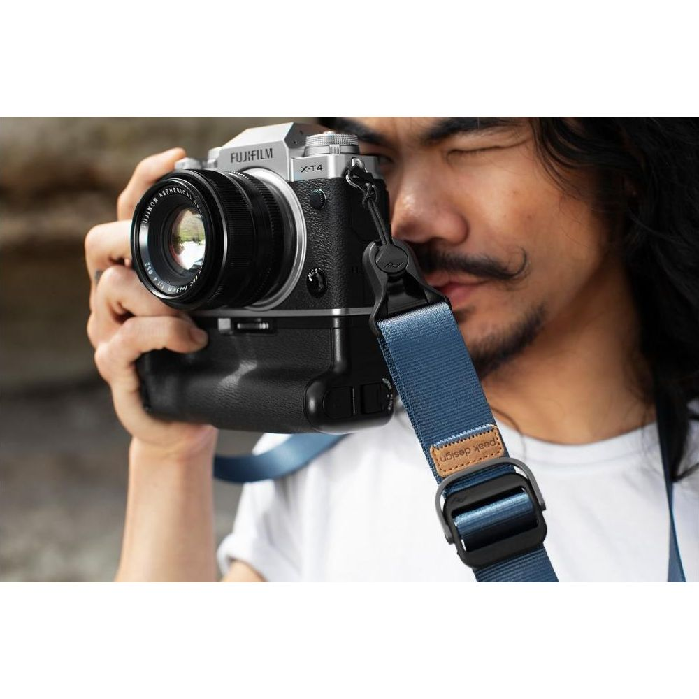 Uomo con fotocamera Fujifilm e tracolla blu Peak Design.