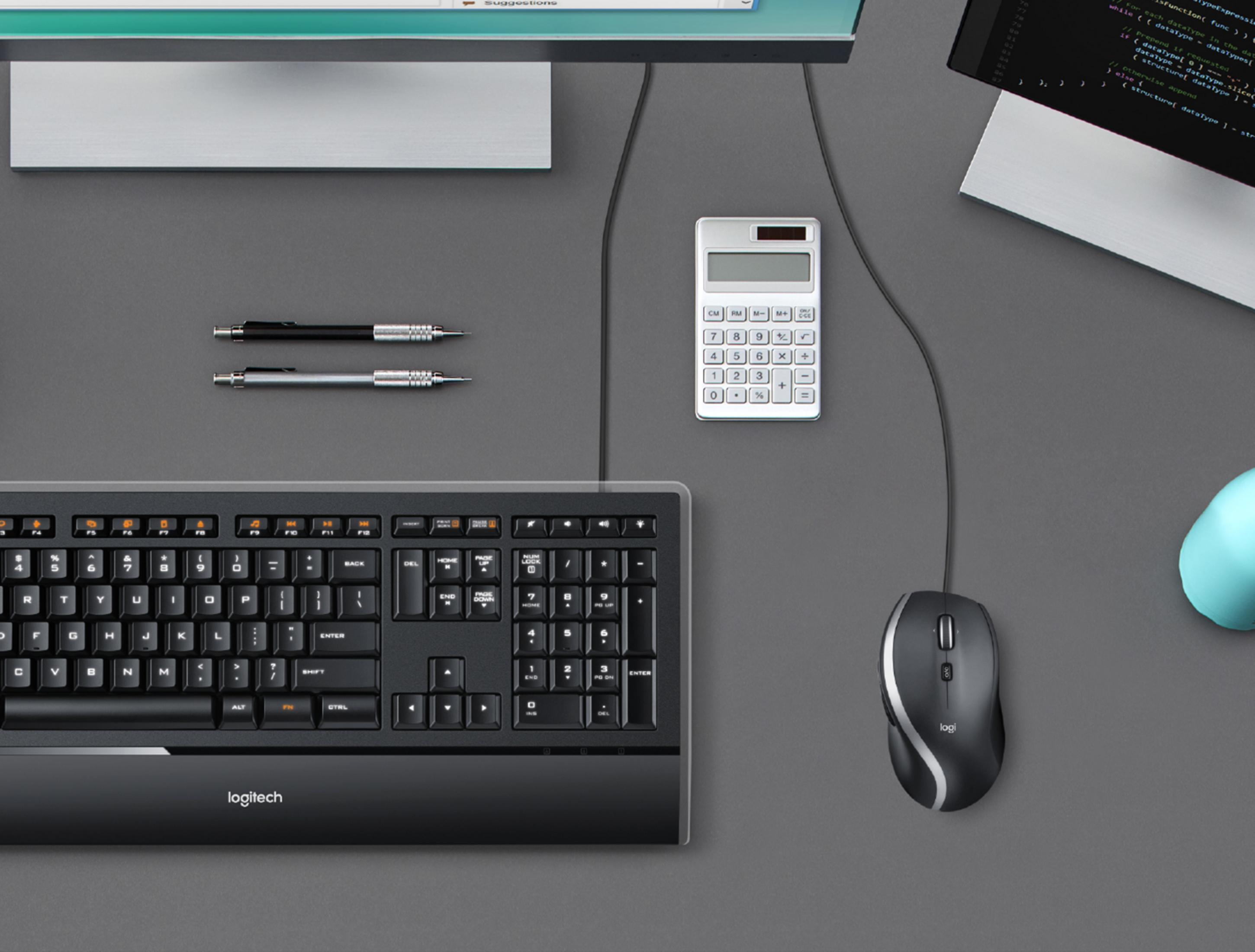 Czarna klawiatura Logitech, mysz, kalkulator, długopisy i monitor.