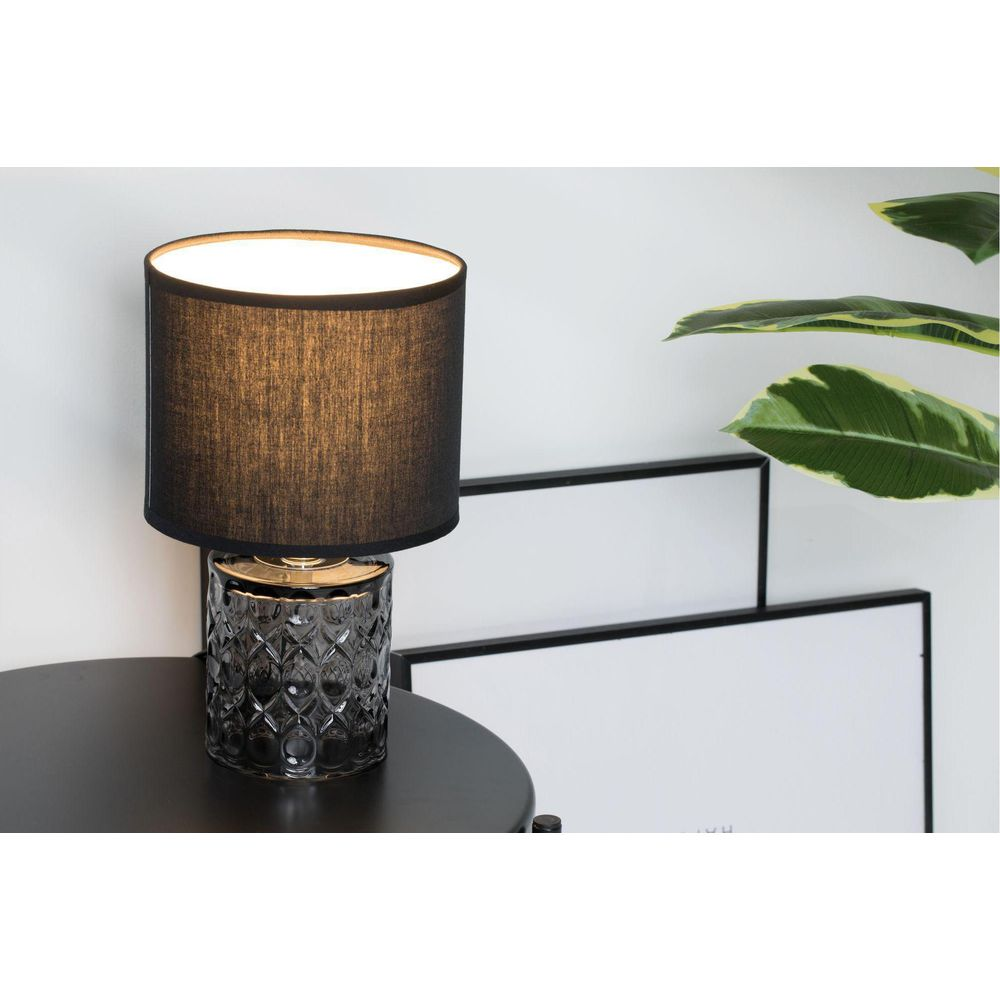 Szara lampa z czarnym kloszem na czarnym stole, obok rośliny.