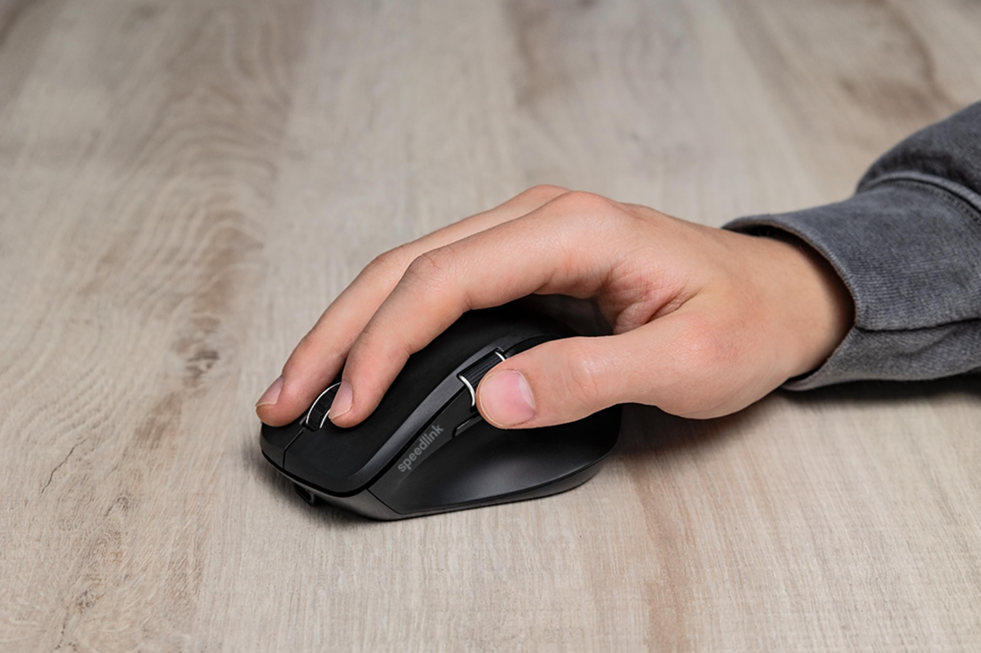 Een hand gebruikt een zwarte Speedlink computermuis op een houten bureau.