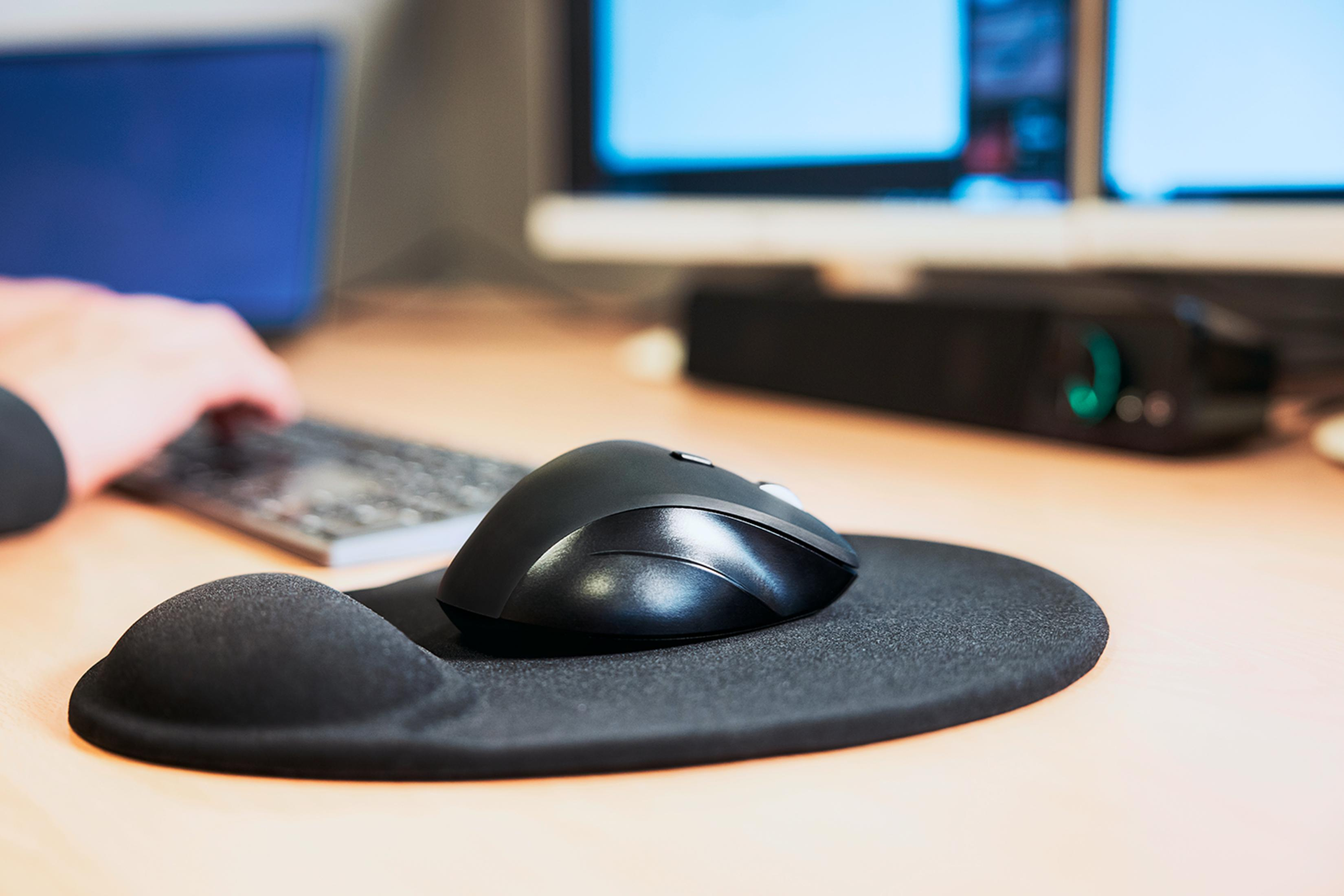 Een zwarte computermuis rust op een zwart polssteunkussen op een bureau.