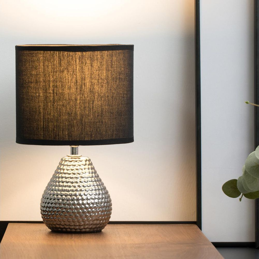 Srebrna lampa z fakturą i czarnym kloszem na drewnie.