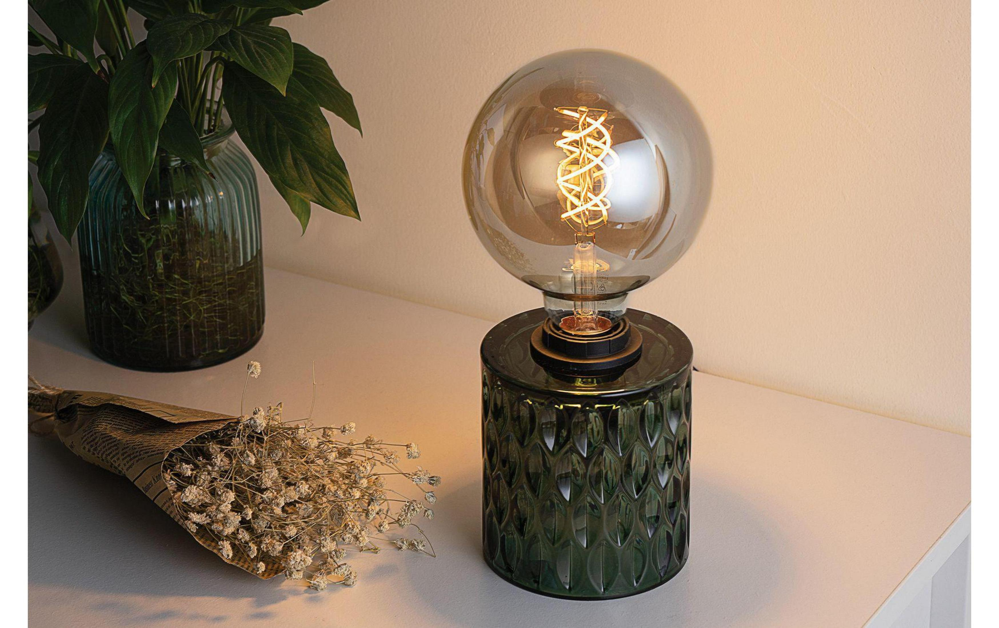 Ciemnozielona lampa z żarówką obok wazonu i suszonych kwiatów.