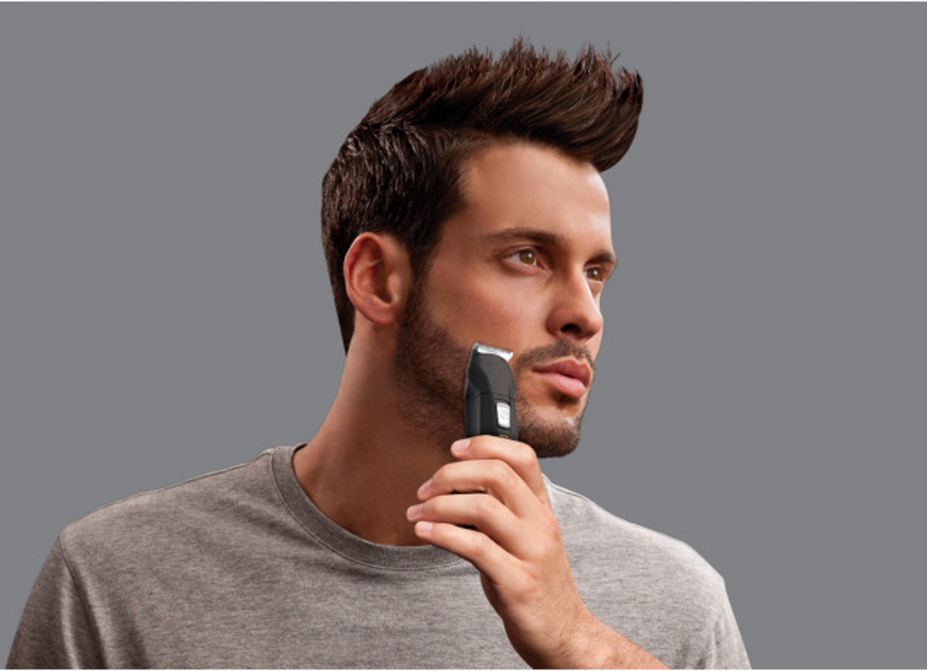 MęŹczyzna przycina zarost trymerem na szarym tle.