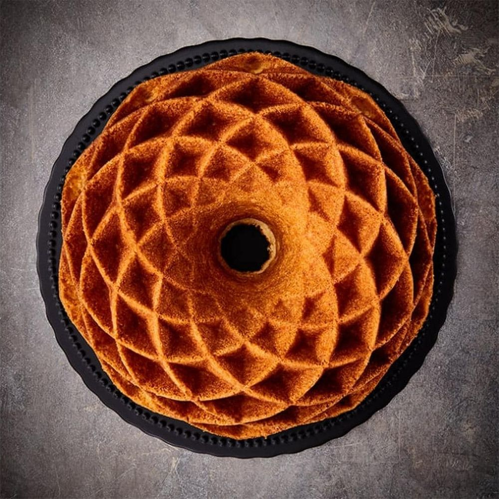 Ein goldbrauner Gugelhupf mit Waffelmuster auf schwarzer Platte, draufsicht.