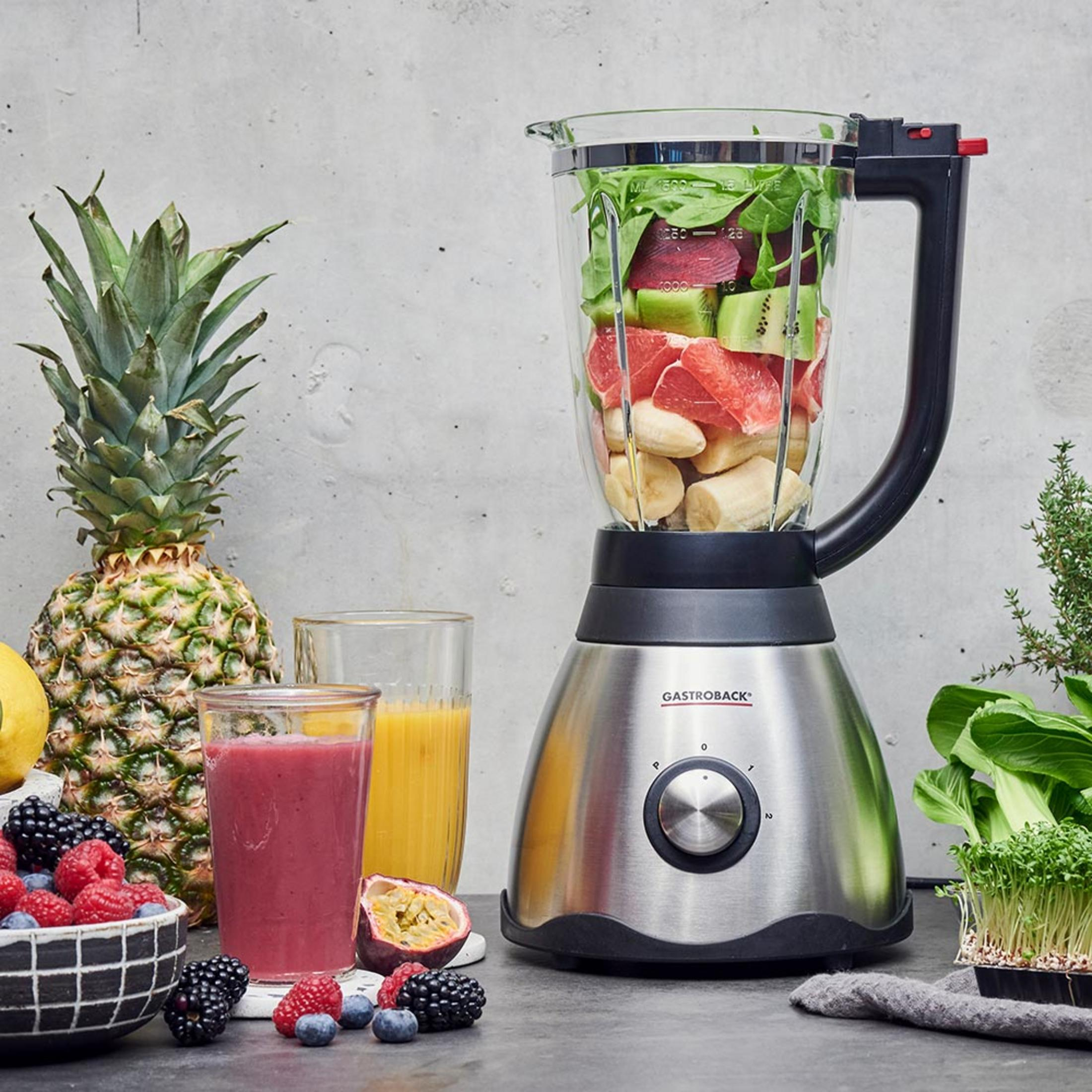 Un frullatore con frutta e verdura, accanto a bacche e un bicchiere di frullato.