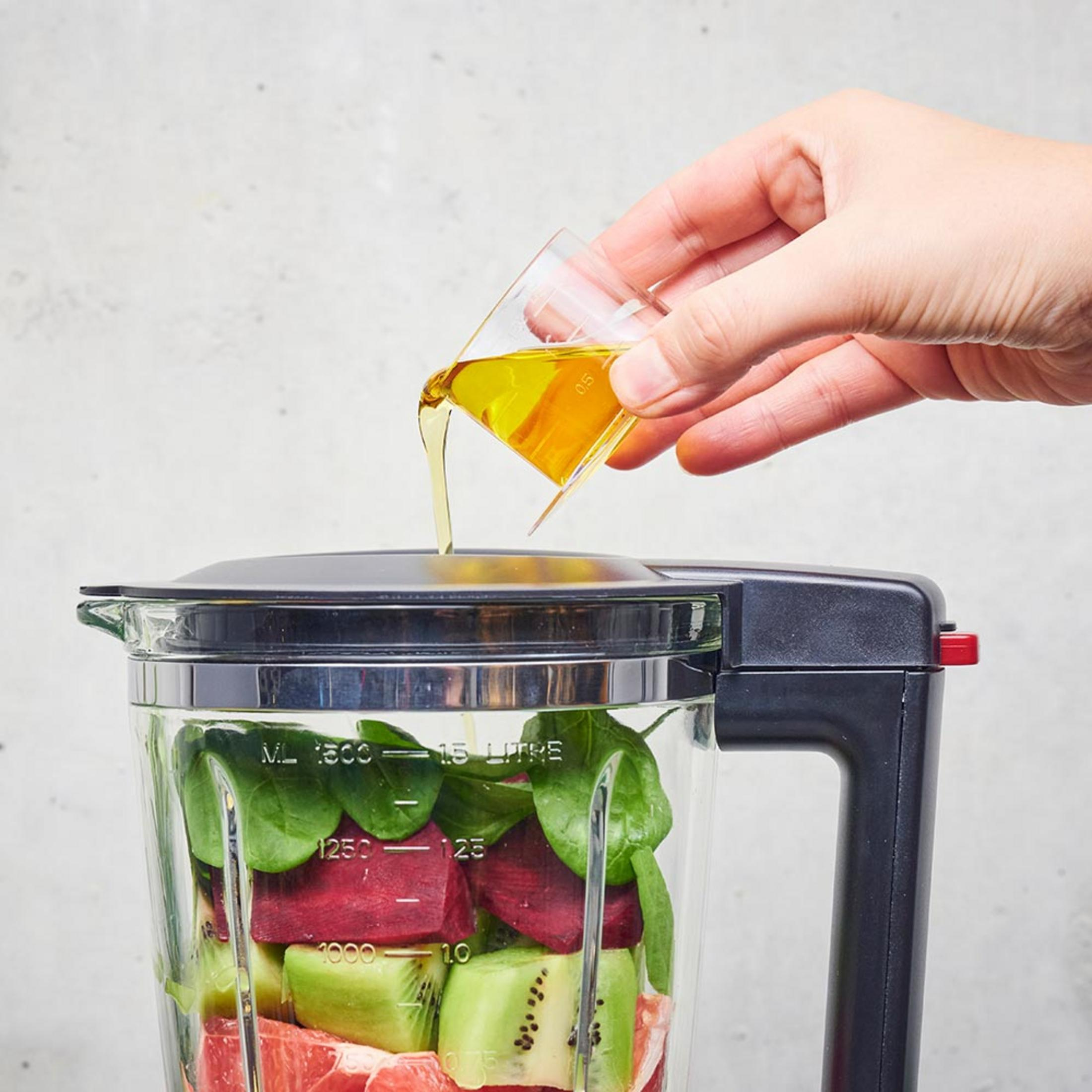 Liquido versato da un bicchierino in un frullatore con frutta.