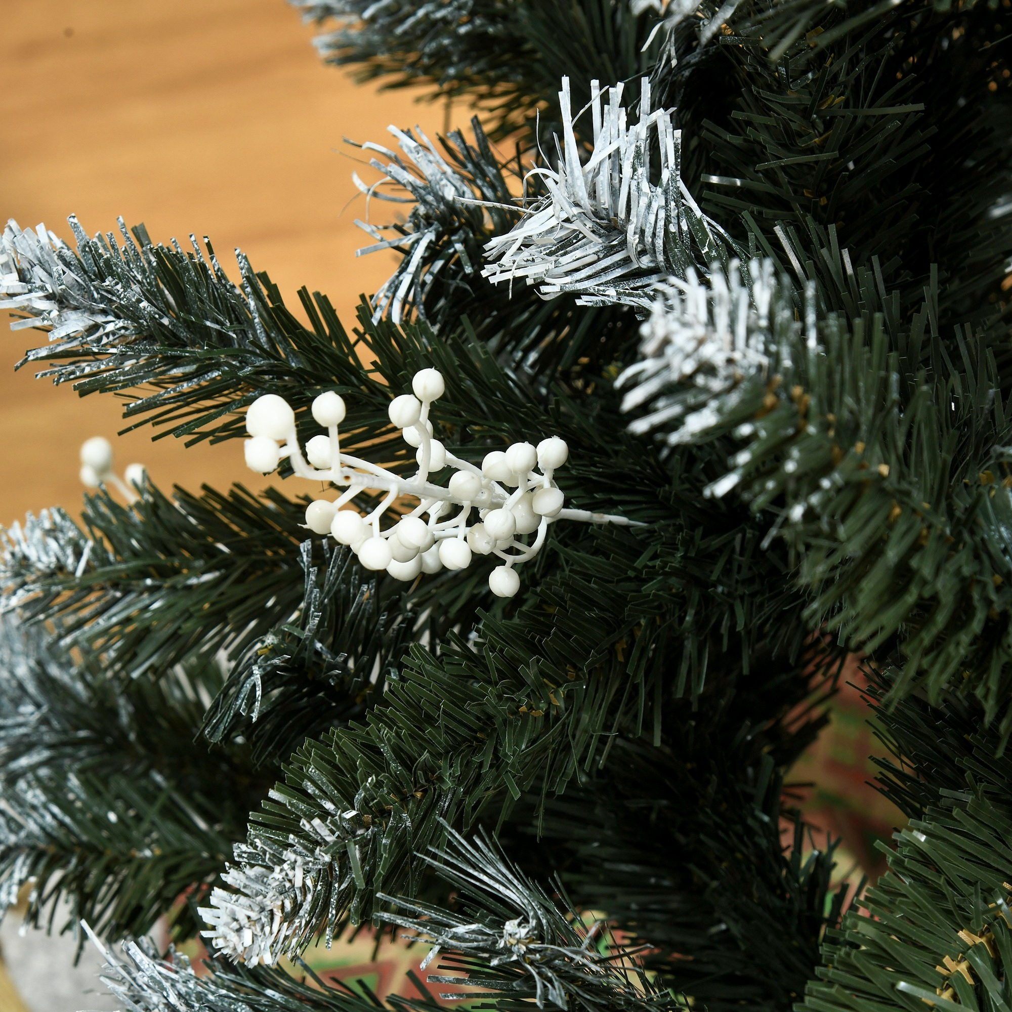 Primer plano de un árbol de Navidad artificial con agujas verdes y bayas blancas.