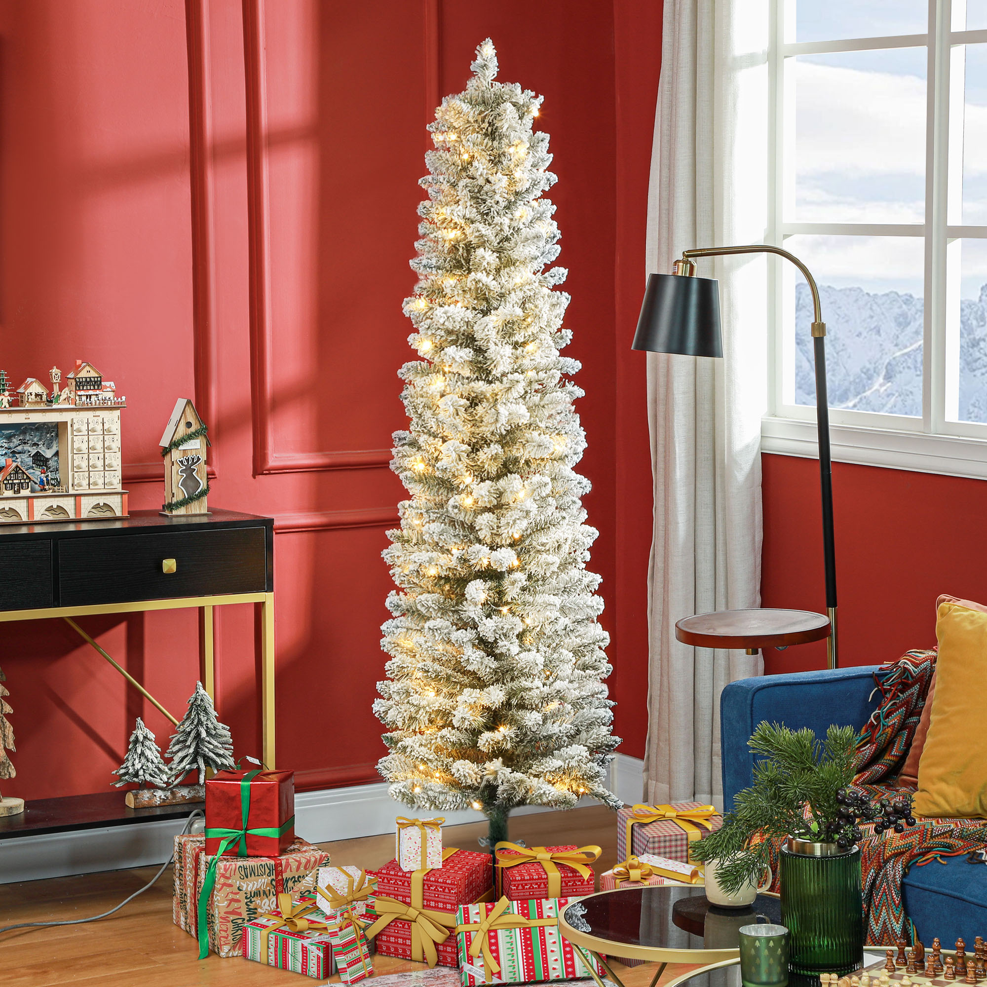 Un árbol de Navidad delgado e iluminado con efecto de nieve en una habitación con paredes rojas.