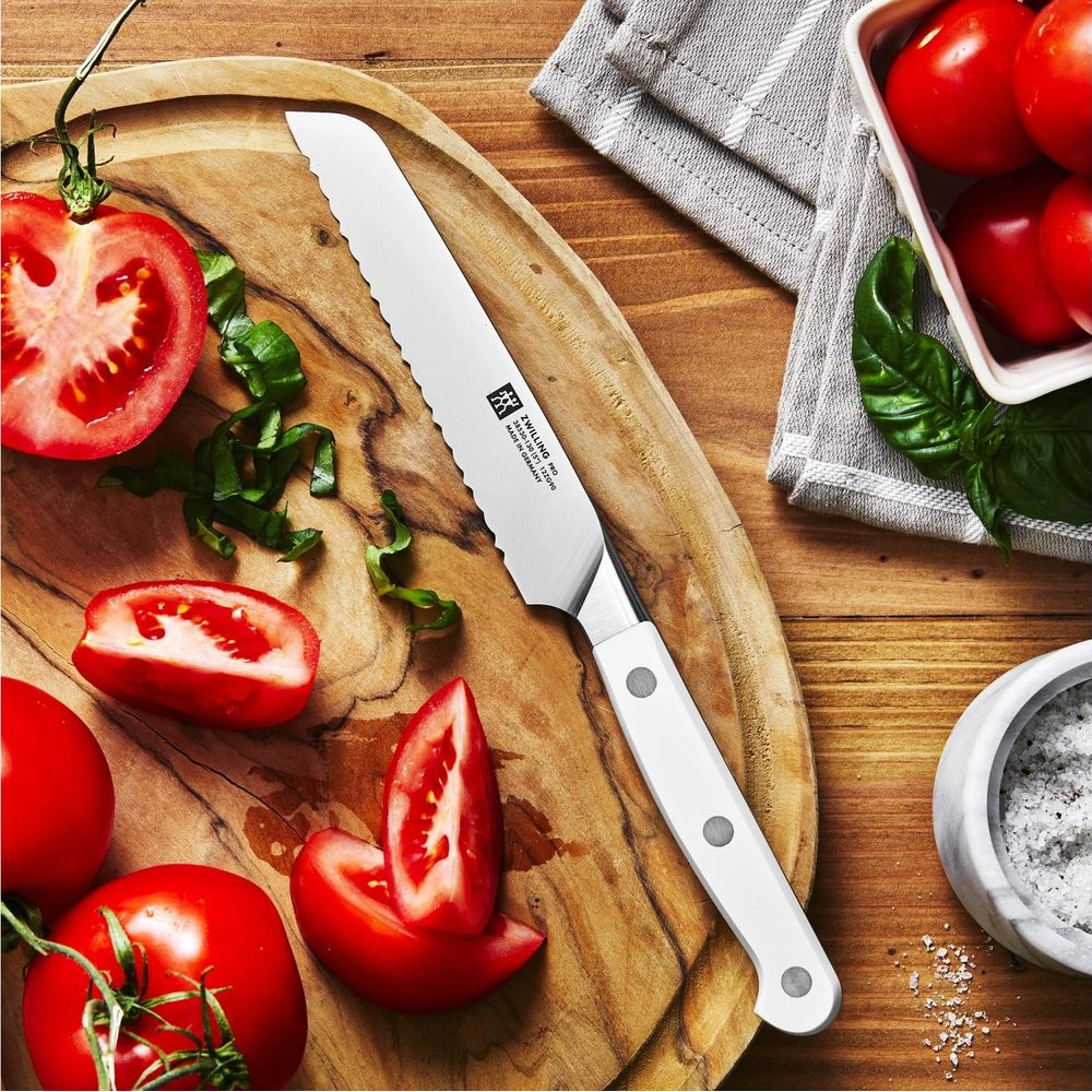 Ein Brotmesser auf einem Holzbrett neben Tomaten und Basilikum.