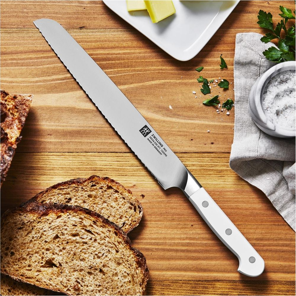Ein Brotmesser liegt auf einem Holztisch neben geschnittenem Brot, Butter und Salz.