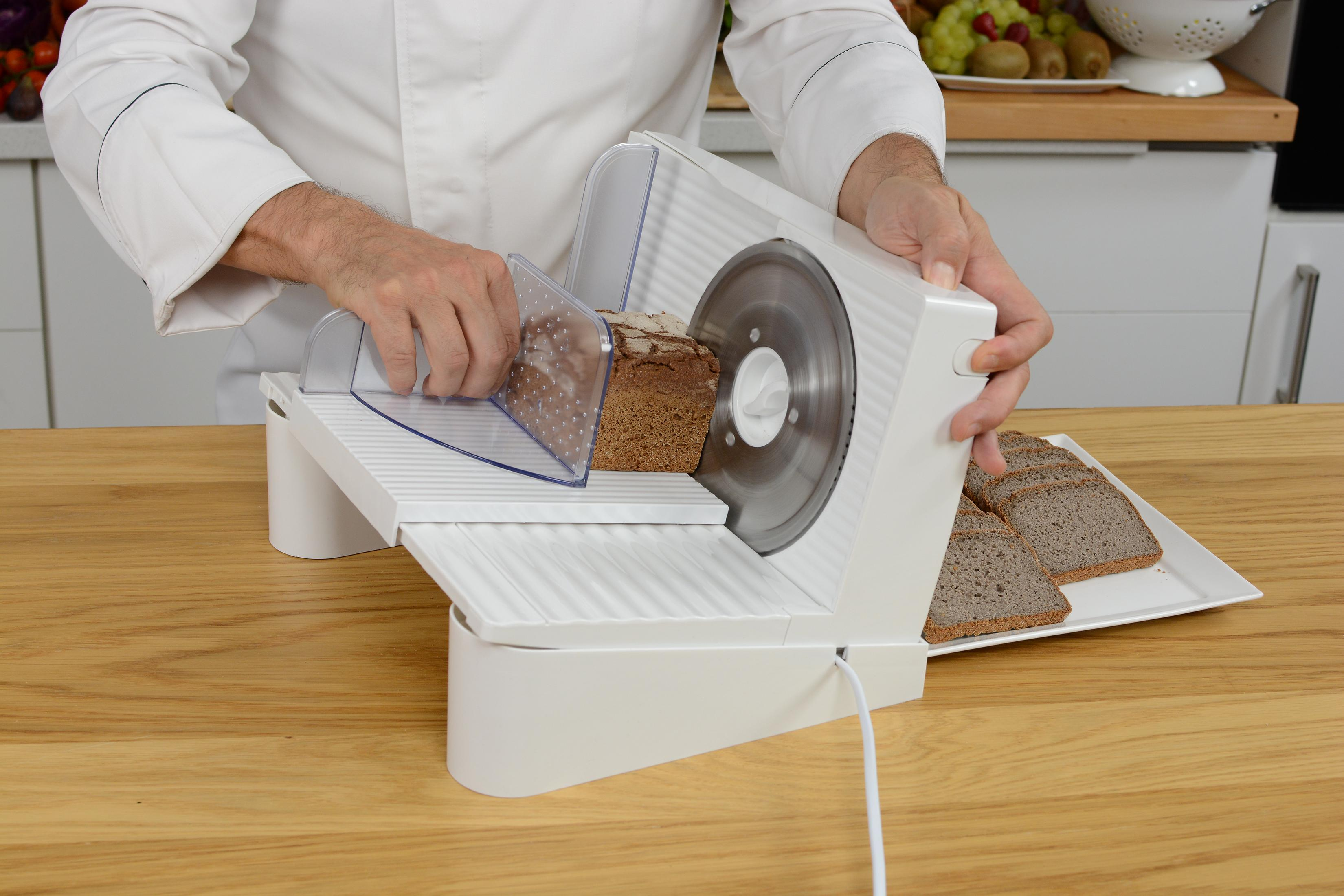 Uno chef affetta il pane con un'affettatrice elettrica in cucina.