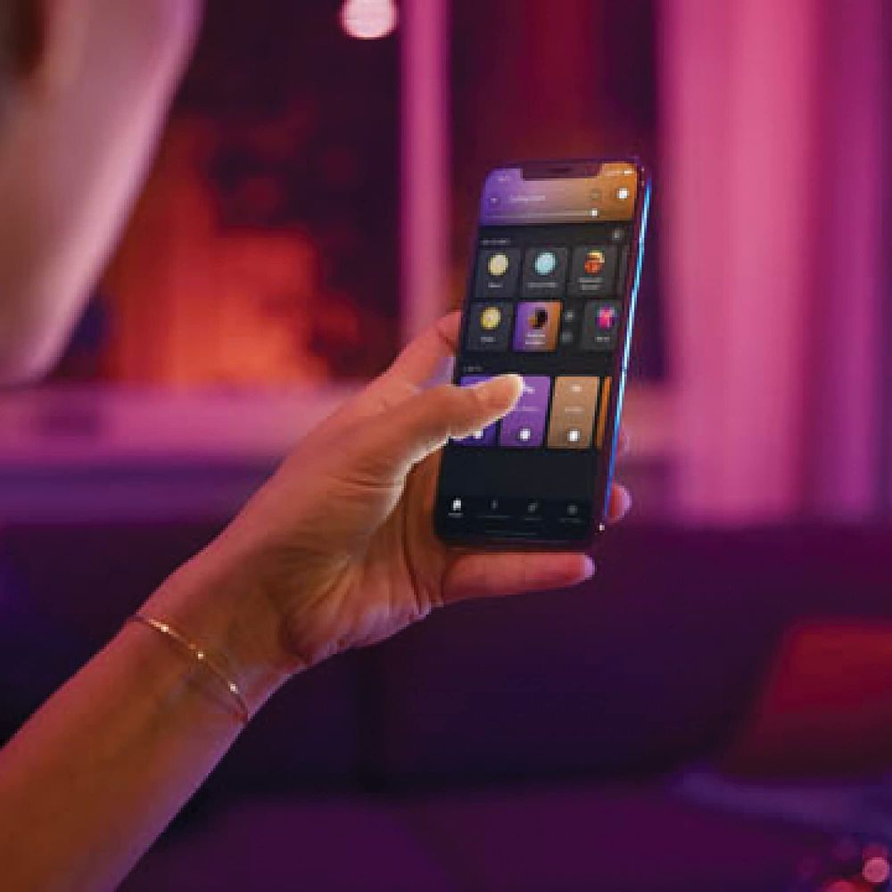 Dłoń trzyma smartfon z aplikacją do sterowania oświetleniem w słabo oświetlonym pomieszczeniu.